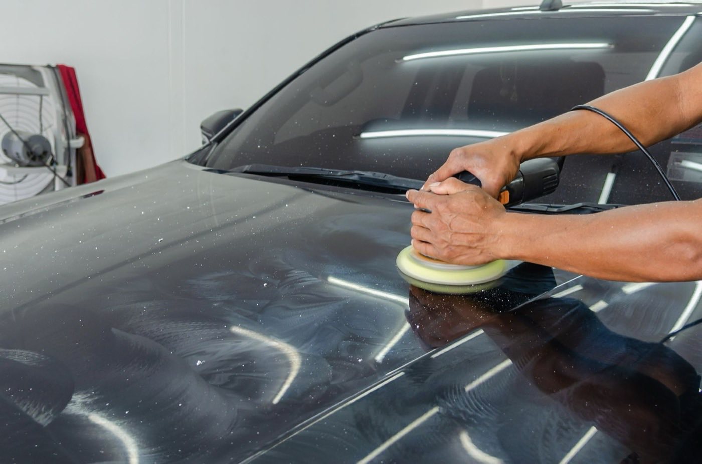 Mão polindo a lataria de um carro preto após reparo